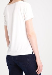 T-shirt bianco a maniche corte realizzato in tessuto leggero, con scollo rotondo, spacchi laterali e vestibilità rilassata.