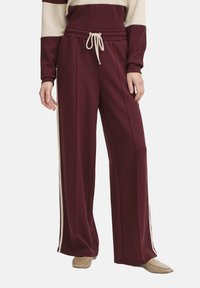 Pantaloni larghi color marrone scuro con vita elasticizzata, chiusura con cordino e strisce laterali crema a contrasto. Tessuto morbido e testurizzato.