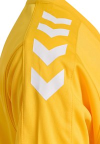 Jersey deportivo amarillo con rayas de chevron blancas en el hombro. Fabricado con un tejido suave, tiene un diseño ajustado y costuras reforzadas.