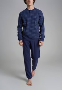 Set di abbigliamento da casa blu navy; felpa con pois blu chiaro e colletto a bottoni, abbinata a pantaloni blu navy. Indossato da un modello.