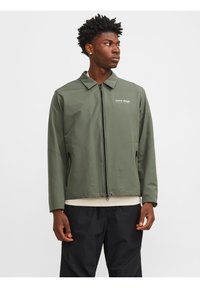 Veste légère verte avec fermeture éclair, manches longues, col pointu, poches latérales et impression du logo sur la poitrine. Texture lisse.
