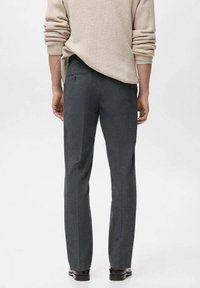 Szare spodnie o dopasowanym kroju, z fakturowanej tkaniny, z detalem w postaci kantów i tylną kieszenią. Noszone z jasnobeżowym swetrem.