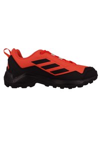 Czerwono-czarne buty sportowe z teksturowaną siateczką, czarną gumową podeszwą z agresywnym bieżnikiem i trzema czarnymi paskami po bokach.