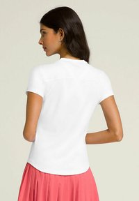 T-shirt bianco a maniche corte con scollatura rotonda e texture liscia, abbinato a una gonna plissettata corallo fluida.