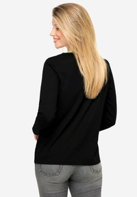 Zwart shirt met lange mouwen en een groene halslijn, gemaakt van katoen. Heeft een relaxte pasvorm en een soepele textuur, gecombineerd met een grijze spijkerbroek.