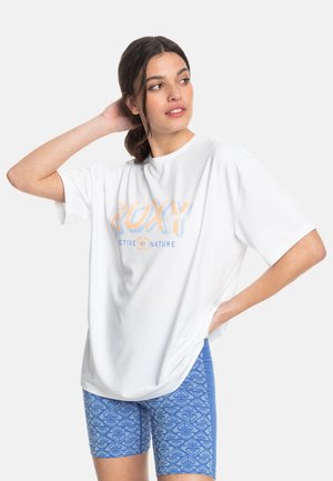 Vit kortärmad T-shirt med "ROXY"-grafik i pastellfärger. Kombinerad med blå mönstrade shorts med geometriska mönster.
