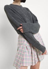 Grauer gestrickter Pullover mit strukturiertem Muster und langen Ärmeln, kombiniert mit einem rosa und grünen Karorock mit Knopfverschluss.