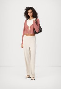 Cárdigan corto de cuadros vichy rojos con lazo, blusa blanca y pantalones de pierna ancha en color crema. Un bolso negro y zapatos en tonos neutros complementan el conjunto.