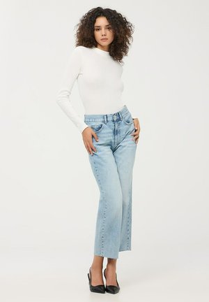 Jeans azzurri a vita alta con una vestibilità rilassata e lunghezza cropped, abbinati a un top fitted bianco a maniche lunghe e tacchi neri.