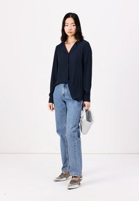 Marineblå langermet bluse med krage, kombinert med lyseblå rette jeans, sølvfargede sko og en sølvfarget clutch-veske.
