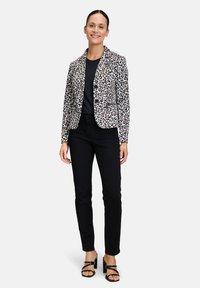 Leopardprint blazer in wit en zwart, met een slim-fit ontwerp en klassieke revers. Gecombineerd met zwarte broek en strapsandalen.