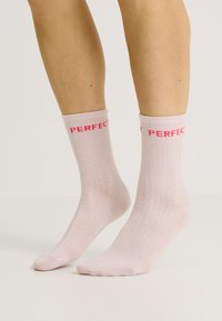 Calcetines de color rosa claro con un tejido suave, que presentan la palabra "PERFECTO" impresa en letras rojas y en negrita alrededor del ribete.