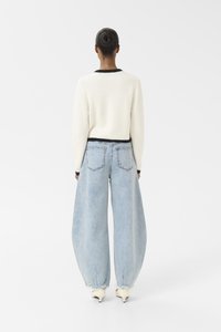 Hvit strikket genser med svart kant, sammen med vide lyseblå denimjeans. Jeansene har en frynset hem og baklommer.