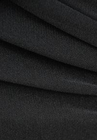 Czarna tkanina o teksturowanej, prążkowanej powierzchni, z wieloma zagnieceniami tworzącymi falisty wygląd. Skupienie na gładkich, ciągłych liniach.