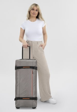 Gray wheeled suitcase with a textured surface, featuring black straps and an orange accent. The handle is extended for easy transport.