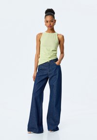 Lys grøn ribbet tanktop parret med brede mørkeblå denimjeans. Tanktoppen har en rund halsudskæring; jeansene har forlommer og synlige sømme.