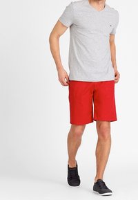 Harmaa lyhythihainen V-kaula-aukkoinen t-paita yhdistetty punaisiin shortseihin. Paidassa on hienovarainen logo ja shortseissa on sileä pinta. Mustat lenkkarit.
