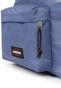 Sac à dos en tissu bleu avec un motif texturé en vagues, featuring une poche avant zippée, un cordon noir, et un patch logo Eastpak.