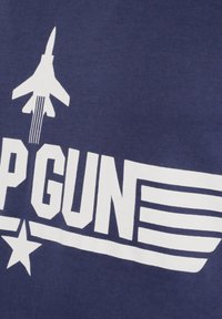 Jaktplansgrafik med motorspår ovanför fet "TOP GUN"-text och en stjärna på mörkblått tygbakgrund.