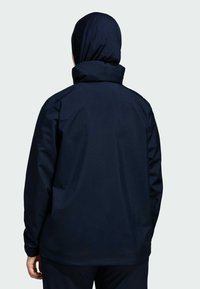 Námornícky modrá vonkajšia bunda s vysokým golierom, dlhými rukávmi a hladkou textúrou. Obsahuje zadný dizajn s minimálnymi detailmi.