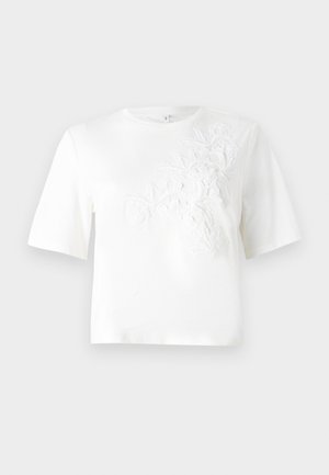 Fehér pamut póló rövid ujjakkal, bal oldalon texturált virágmintás hímzéssel. Kerek nyakkivágás, laza fazon.