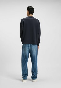 Marinblå sweatshirt med en avslappnad passform, i kombination med ljusblå randiga jeans. Har en rund hals och ribbade ärmslut.