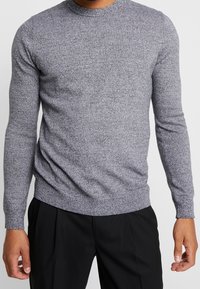 Szary sweter z okrągłym dekoltem, długi rękaw, wykonany z fakturowanej dzianiny. Ma ściągacze u dołu i na mankietach, co zapewnia dopasowane wykończenie.