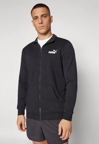 Black zip-up hoodie, cotton material, ribbed cuffs and hem, front pockets, features white Puma logo on left chest, plain design, relaxed fit.