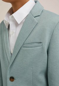 Ljusblå strukturerad kavaj med en enkel knappstängning, notched lapels och en bröstficka, matchad med en vit skjorta med krage under.