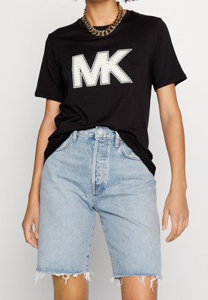 Zwart T-shirt met een groot wit "MK" logo met studaccenten, gecombineerd met lichtblauwe denim shorts met rafelige randen.