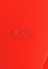 Gros plan sur un tissu rouge avec un logo de crocodile brodé assorti à la couleur du tissu.
