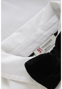 Witte shirtkraag met een getextureerde zwarte fluwelen strikaccent. Label leest "91 luiers," wat merk en maat aangeeft. Zacht, glad materiaal.