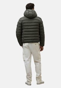 Gepolsterte, mit Kapuze versehene Jacke in Dunkelgrün mit einem gesteppten Design; kombiniert mit hellen Cargo-Hosen mit seitlichen Taschen.