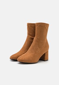 Bruine suède enkellaarsjes met een spitse neus en een chunky blokhak, met een soepele textuur en minimale stikdetails.