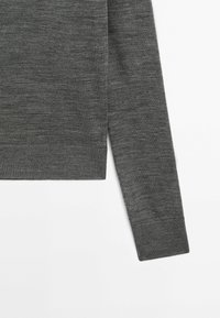 Pull gris en maille avec un col rond, des manches longues et un ourlet côtelé. Le tissu a une texture douce avec un design léger.