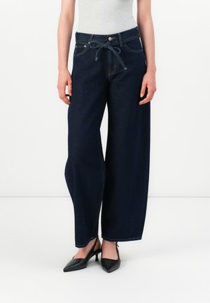 Jeans in denim scuro a gamba larga con vita regolabile, tasche frontali e cuciture a contrasto. Abbinati a scarpe con tacco a punta nere.