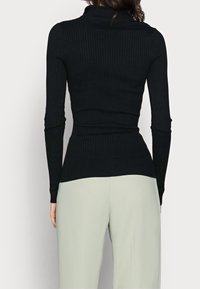 Haut noir côtelé à manches longues avec un col roulé, une silhouette ajustée et un tissu texturé. Associé à un pantalon vert clair.