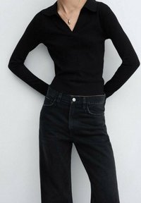 Top negro de manga larga con cuello, combinado con jeans de mezclilla negros de cintura alta que cuentan con bolsillos frontales y un detalle de botón plateado.