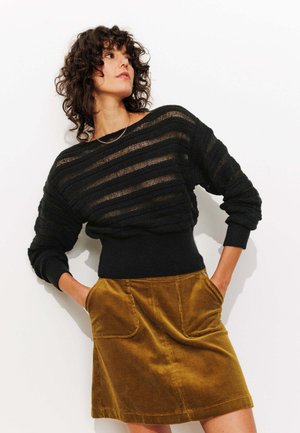 Pull en tricot à rayures noires avec une finition texturée, associé à une jupe en velours côtelé moutarde, dotée de deux poches avant.