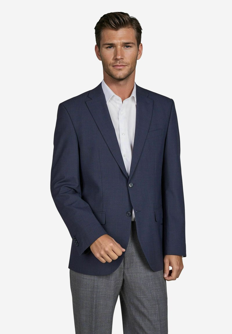 Navyblauwe maatblazer met schouderflappen, twee knopen en voorkeurszakken, gecombineerd met een witte blouse en grijze gestructureerde broek.