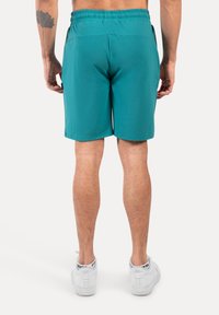Pantalones cortos deportivos turquesa con cintura elástica, que cuentan con un bolsillo lateral y una textura de tela suave. Se llevan con zapatillas blancas.