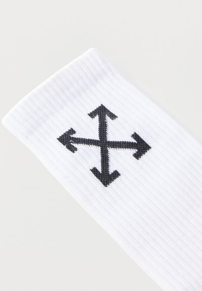 Tissu blanc à côtes avec un symbole fléché noir à quatre directions brodé au centre, indiquant les directions haut, bas, gauche et droite.