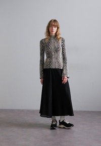 Maglietta a maniche lunghe con un motivo zigzag bianco e nero, abbinata a una gonna nera fluida e scarpe da ginnastica nere. Tessuto liscio con texture a coste.