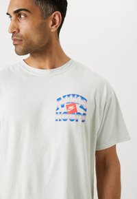 Lys grå bomulds t-shirt med et flerfarvet "NIKE HOOPS" logo på venstre bryst. Korte ærmer og rund hals.