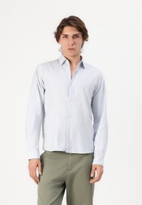Camisa de manga larga azul claro con finas rayas blancas, cierre frontal de botones y un cuello clásico. Fabricada con una tela texturizada.