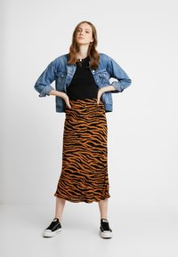 Schwarz-orange gestreifter Rock in Tigeroptik, gefertigt aus einem weichen, dehnbaren Stoff, kombiniert mit einem schwarzen Oberteil und einer Jeansjacke, abgerundet mit schwarzen Sneakers.