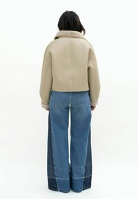 Beige cropped jack met een schapenvacht kraag, gecombineerd met wide-leg denim jeans met contrasterende blauwe panelen en stikseldetails.