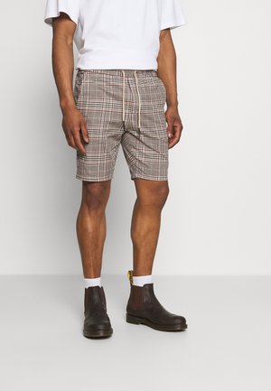 Pantalones cortos de cuadros marrones con cintura elástica y cordón; combinados con calcetines blancos y botas de cuero marrón hasta el tobillo.