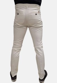 Jeans bianchi a taglio slim con tasche posteriori, leggermente elasticizzati e con una texture liscia. Abbinati a sneakers nere a scacchi.