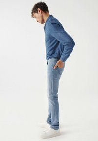 Plava traper košulja s dugim rukavima i džepom na prsima, u kombinaciji sa svijetloplavim trapericama. Bijele tenisice upotpunjuju ležernu odjeću.